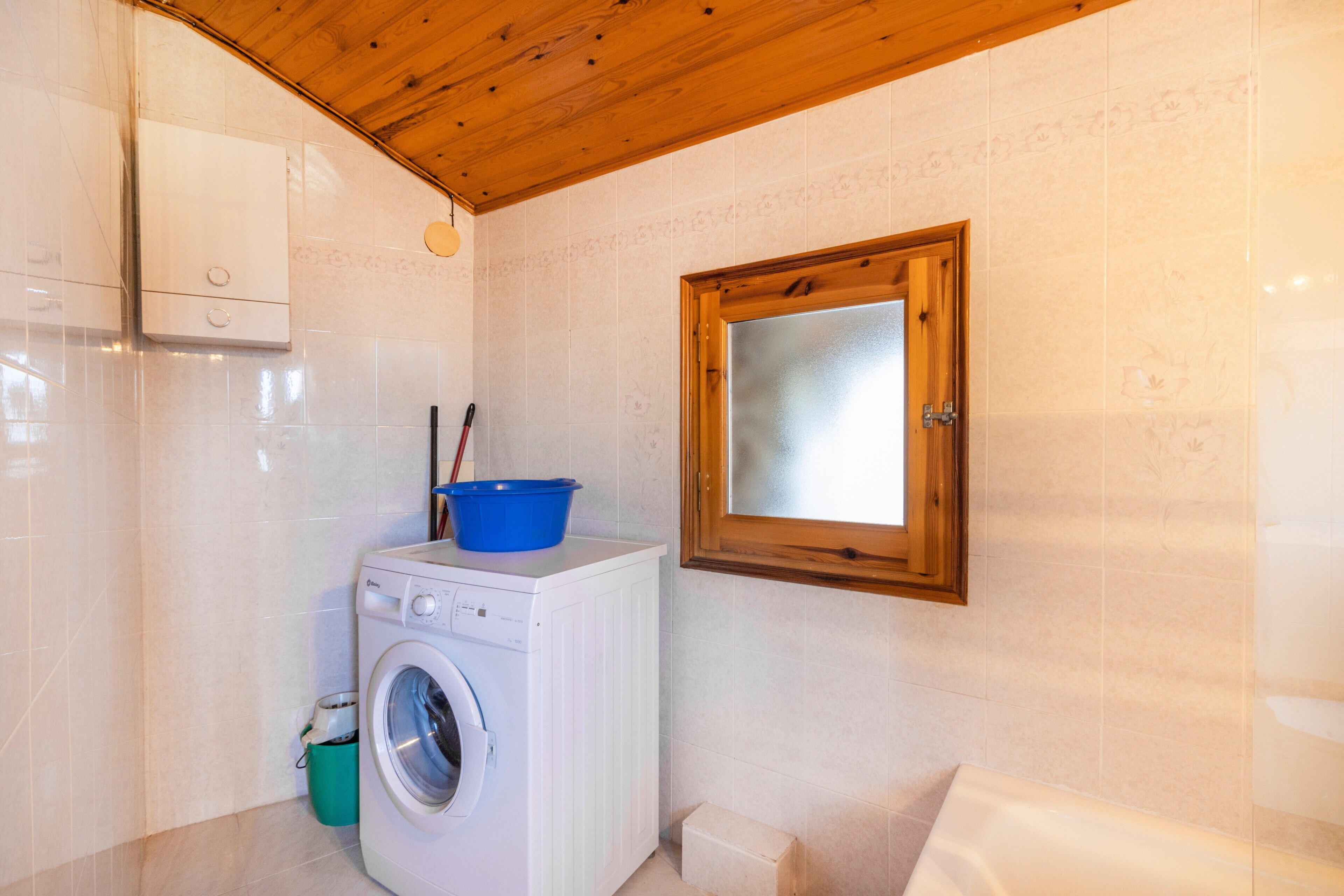 A laundry area with a washing machine, a blue basin, and a wooden-framed window.
