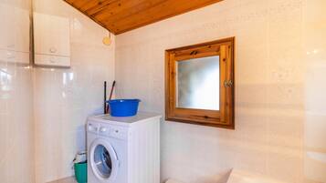 A laundry area with a washing machine, a blue basin, and a wooden-framed window.