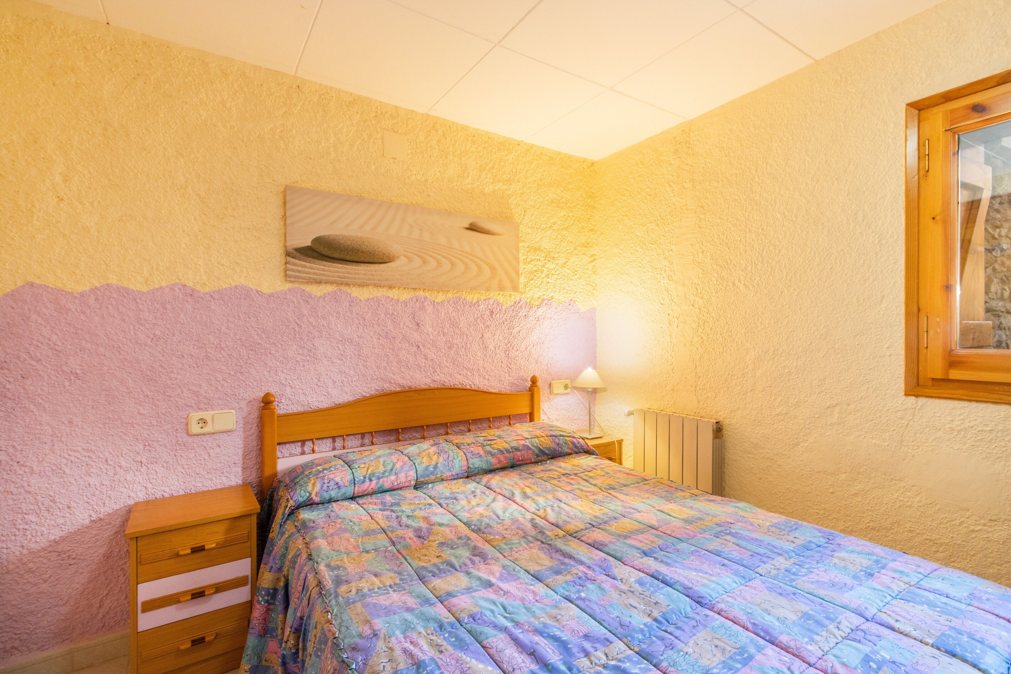 Un dormitorio con una cama, una mesita de noche de madera, una lámpara de pared y un radiador.