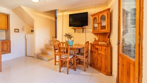 Un comedor con una mesa y sillas, un televisor montado en la pared, armarios de madera y una escalera que lleva a otro nivel.