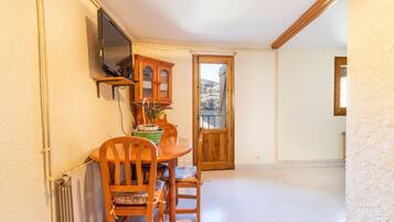 A dining area with a wooden table and chairs, a potted plant, and a wooden cabinet with a television mounted on the wall.