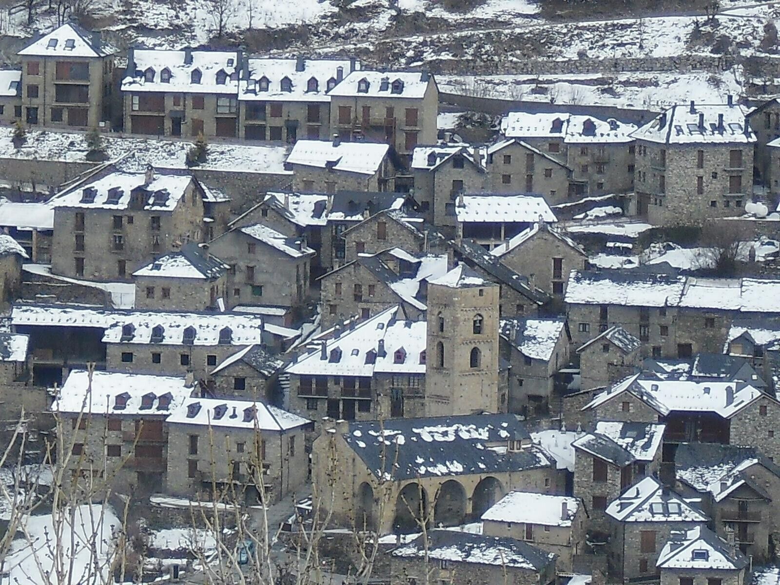A cluster of stone buildings with multiple roofs, some with towers, in a snowy landscape.
