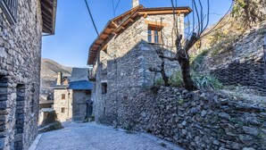 Un edificio de piedra con un balcón de madera, una calle adoquinada y montañas al fondo.