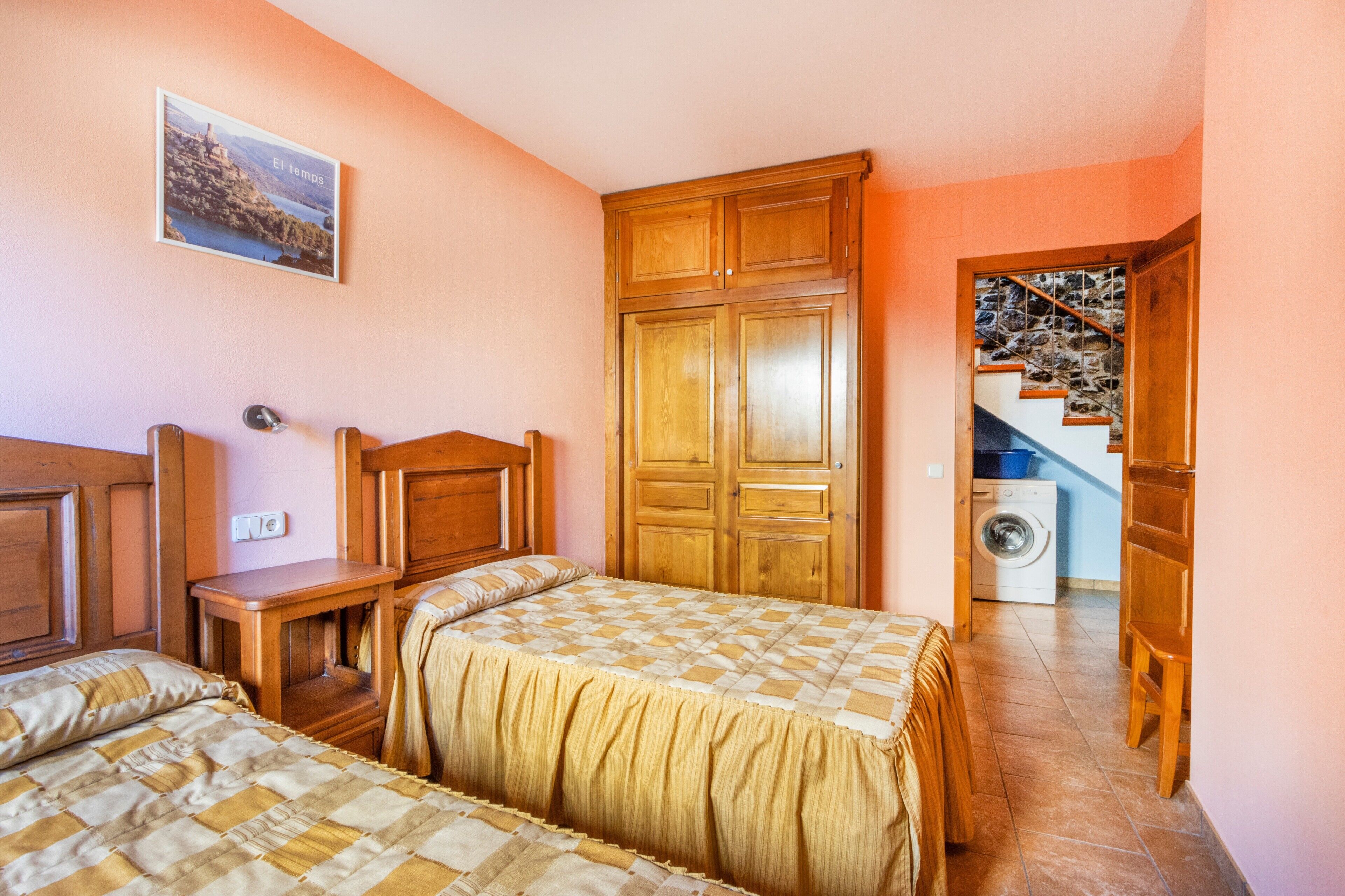 Une chambre avec deux lits, une armoire en bois, un lave-linge et un escalier.