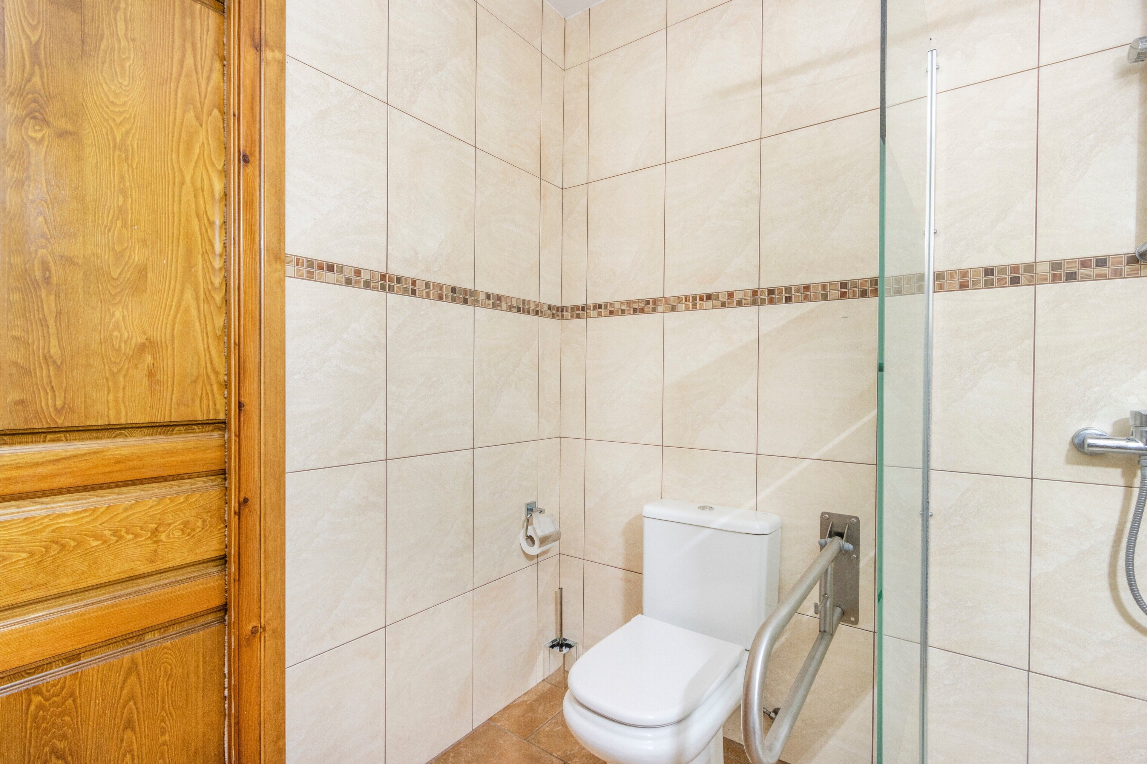A bathroom with a wooden door, a toilet, a glass shower enclosure, and a tiled floor.
