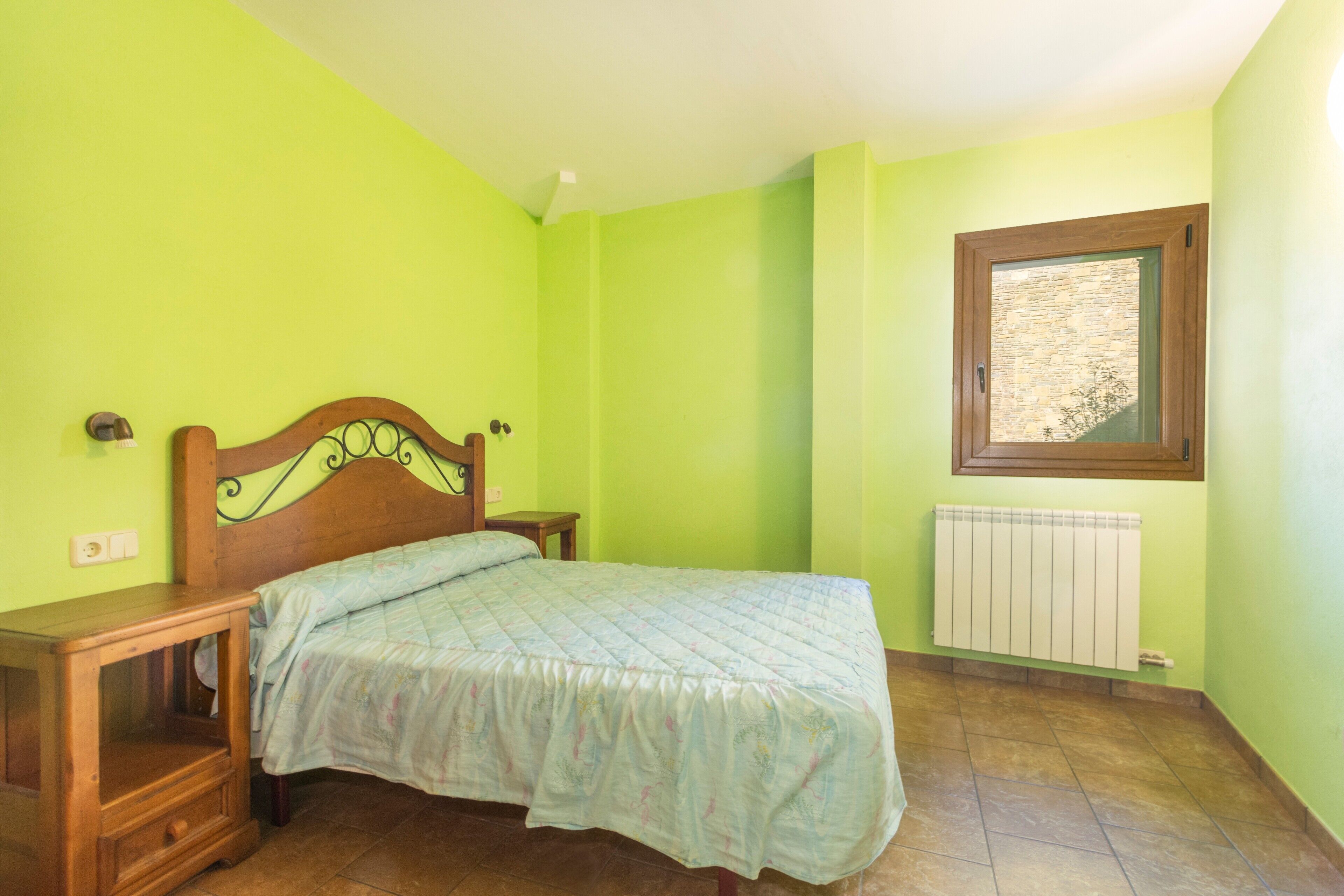 Een slaapkamer met een bed, nachtkastje, raam en een radiator.