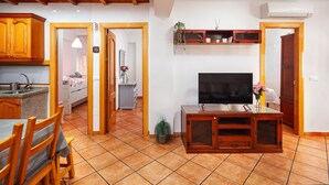 Un salon avec un téléviseur, des meubles en bois, un coin repas avec des chaises et une cuisine avec un évier.