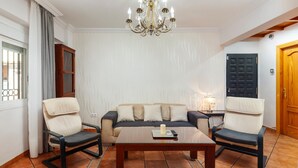Un salon comprenant un canapé, deux fauteuils, une table basse, un lustre, un meuble et une porte.