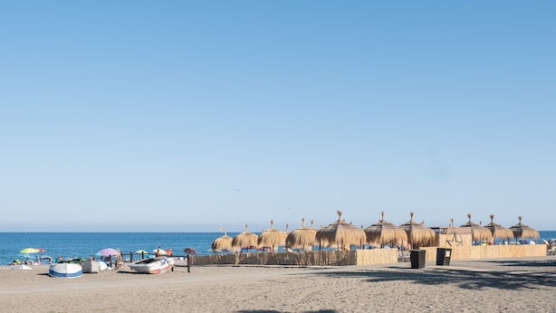 Une plage avec des parasols en chaume, des bateaux et un ciel dégagé.