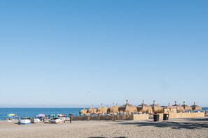 Une plage avec des parasols en chaume, des bateaux et un ciel dégagé.