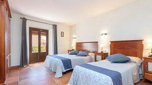 Une chambre d’hôtel avec deux lits, une tête de lit en bois, une porte avec des rideaux et un sol carrelé.