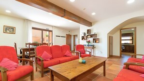 Un vaste espace de vie avec un canapé rouge, des chaises en bois, une table basse en bois et une cuisine en arrière-plan.