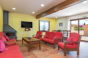 A living room with a fireplace, red furniture, a television, and a window with a view. - Cottage 'Can Centena' with Private Pool, Wi-Fi and Air Conditioning (Vilamacolum)