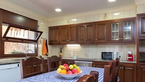 Une cuisine avec des meubles en bois, une table à manger recouverte d’une nappe à carreaux et un saladier rempli de fruits.