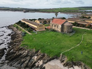 Une propriété située sur la côte, avec un bâtiment en pierre, une pelouse verdoyante et un sentier menant à la mer.