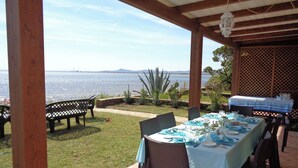 An outdoor patio with a table set for dining, overlooking a body of water. - HOUSE ON THE SEA, WATERFRONT, BREATHTAKING VIEW WITH GARDEN AND PRIVATE BEACH (STINTINO)