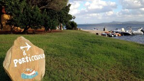 A stone sign with 'Porticciolo' and a boat illustration, grassy area, trees, and boats by the water. - HOUSE ON THE SEA, WATERFRONT, BREATHTAKING VIEW WITH GARDEN AND PRIVATE BEACH (STINTINO)