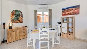 Un comedor con una mesa dispuesta para cuatro, un armario de madera, un estante con espacio de almacenamiento y un cuadro en la pared.
