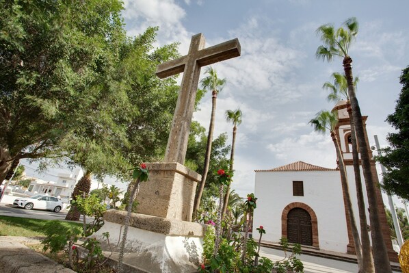 A cross monument, a church with a bell tower, and palm trees.