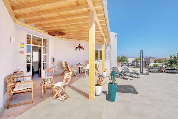 Un patio al aire libre con mobiliario de madera, plantas en macetas y una vista despejada del paisaje circundante.