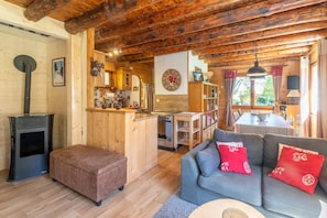 Acogedor interior de cabaña con detalles de madera, una kitchenette, un comedor y una sala de estar con sofá y reposapiés.
