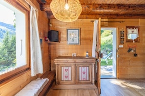 A wooden cabin interior with a wooden cabinet, a hanging light fixture, a framed picture, and a door leading outside. - Chalet "Le Petit Ranch" with Mountain View and Private Garden (Le Reposoir)