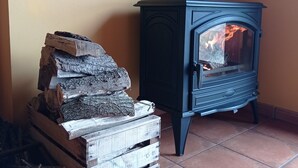 A room with a wood-burning stove, a stack of firewood, and a tiled floor.