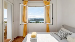 A bedroom with a bed, a window with curtains, a view of a landscape, and a door. - Apartment 'Appartement Avec 2 Piscines' with Sea View, Wi-Fi and Air Conditioning (Mutxamel)