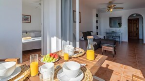 A dining area with a table set for breakfast, a sofa, and a ceiling fan in the background. - Apartment 'Appartement Avec 2 Piscines' with Sea View, Wi-Fi and Air Conditioning (Mutxamel)