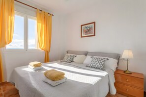 A bedroom with a bed, a nightstand, a lamp, a window with curtains, and a framed picture on the wall. - Apartment 'Appartement Avec 2 Piscines' with Sea View, Wi-Fi and Air Conditioning (Mutxamel)