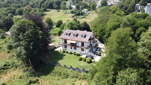 An aerial view of a two-story house with a sloped roof, surrounded by dense greenery and a well-maintained lawn.