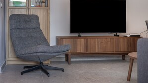 A modern living room with a grey office chair, a flat-screen TV, and a wooden cabinet. - Apartment 'Ático San Jose' with Shared Terrace, Wi-Fi and Air Conditioning (Cádiz)