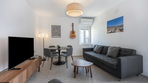 A modern living room with a flat-screen TV, a grey sofa, a dining table with chairs, a guitar, a pendant light, and a painting on the wall. - Apartment 'Ático San Jose' with Shared Terrace, Wi-Fi and Air Conditioning (Cádiz)
