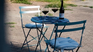 Ein Tisch mit zwei Weingläsern und einer Flasche, umgeben von blauen Stühlen mit Kissen.