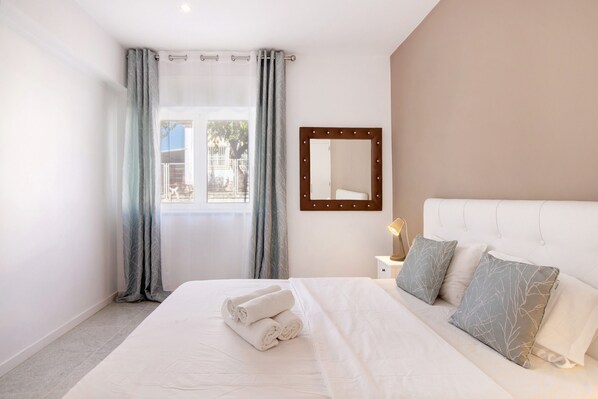 A hotel room with a bed, a large mirror, and a window with curtains.