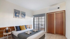 A bedroom with a bed, nightstand, lamp, artwork, and sliding closet doors. - Sousa E Filhos Apartment – Shared Pool, Near the Beach (Albufeira)