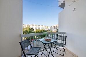 A balcony with a table and chairs, a potted plant, and a view of buildings in the background. - Sousa E Filhos Apartment – Shared Pool, Near the Beach (Albufeira)