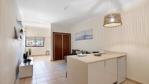A modern kitchen with a central island, a dining area with a sofa, and a view through a window. - Sousa E Filhos Apartment – Shared Pool, Near the Beach (Albufeira)