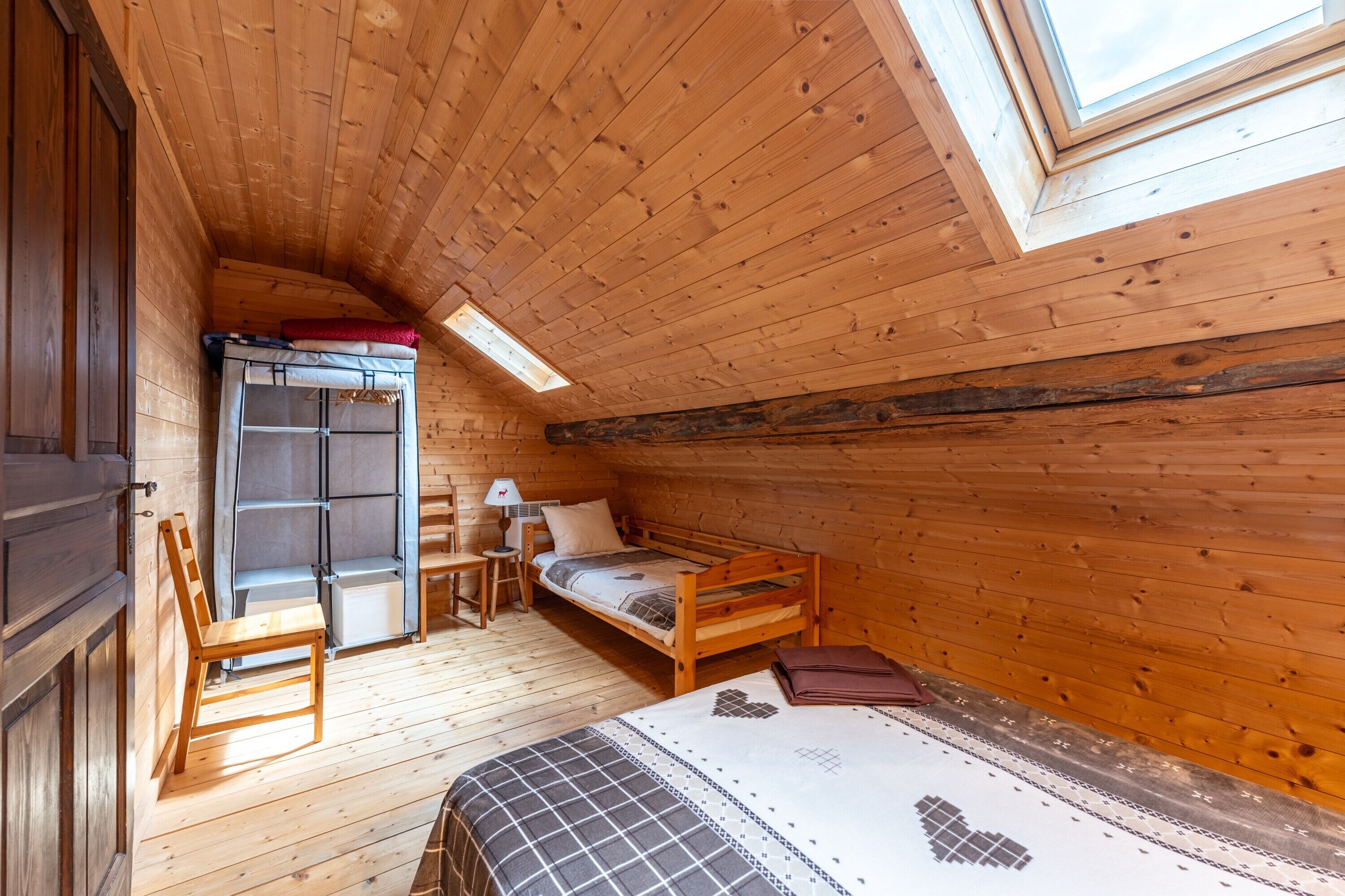 A wooden room with a bed, a chair, a desk, and a wardrobe.