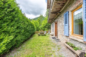 A stone building with a wooden deck, a picnic table, and a well-maintained garden. - Apartment "Le Grand Tétras" with Shared Terrace, Balcony, and Wi-Fi (Flumet)