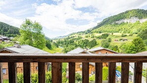 Ein Holzbalkon mit Blick auf eine gebirgige Landschaft, darunter Häuser und Grünpflanzen.