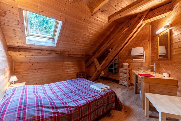 A wooden cabin bedroom with a bed, a desk, a dresser, and a skylight.