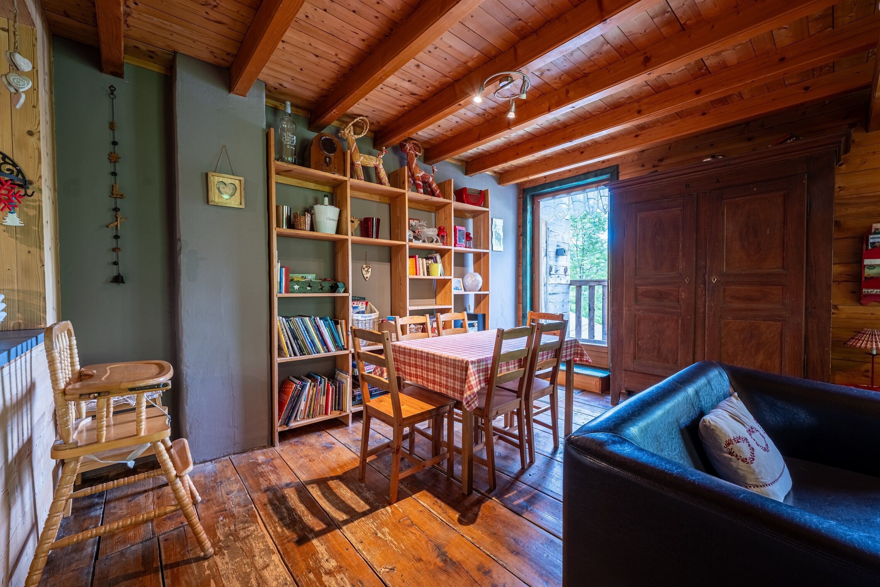 A cozy room with wooden floors, a dining table with chairs, a bookshelf, and a large wardrobe.