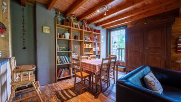 A cozy room with wooden floors, a dining table with chairs, a bookshelf, and a large wardrobe.