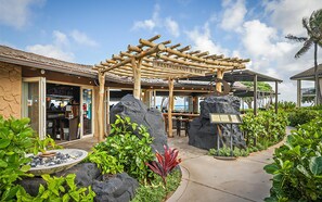A restaurant with a wooden pergola, outdoor seating, and a view of the ocean.