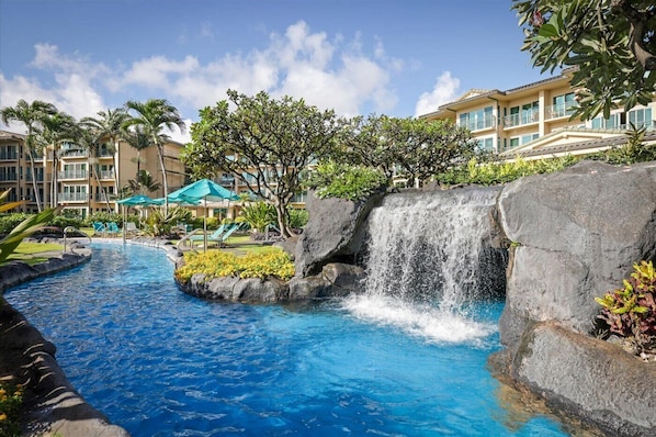 A hotel with a swimming pool, a waterfall, and a building with balconies.