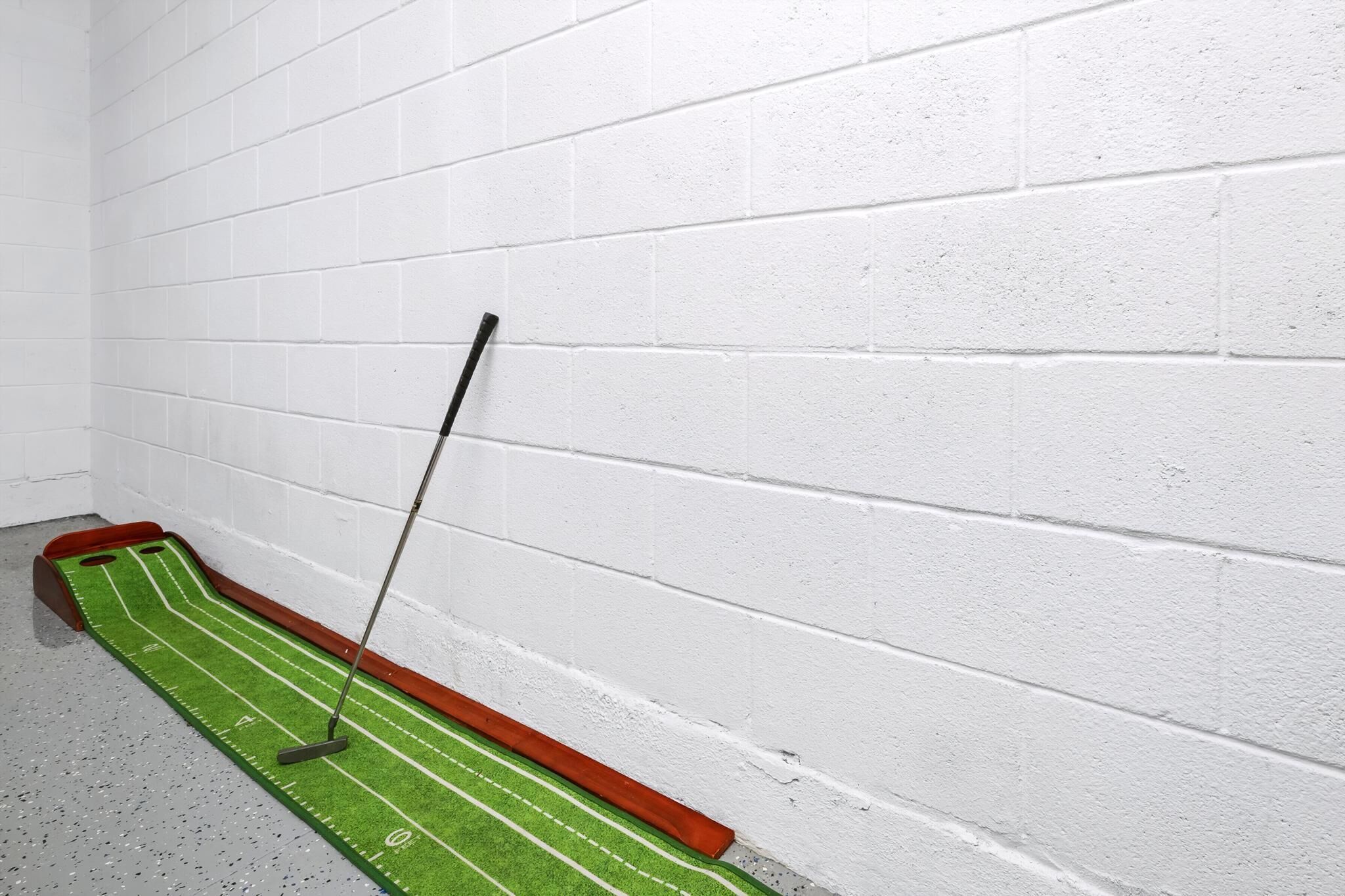 A green and red indoor croquet mat against a white brick wall.