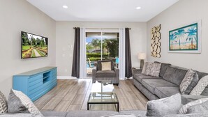 A modern living room with a sofa, a coffee table, and a TV mounted on the wall. There is a sliding glass door leading to an outdoor area with a pool. - Spacious Home near Disney: Waterpark, Themed & Game Room - 341PN (Kissimmee)