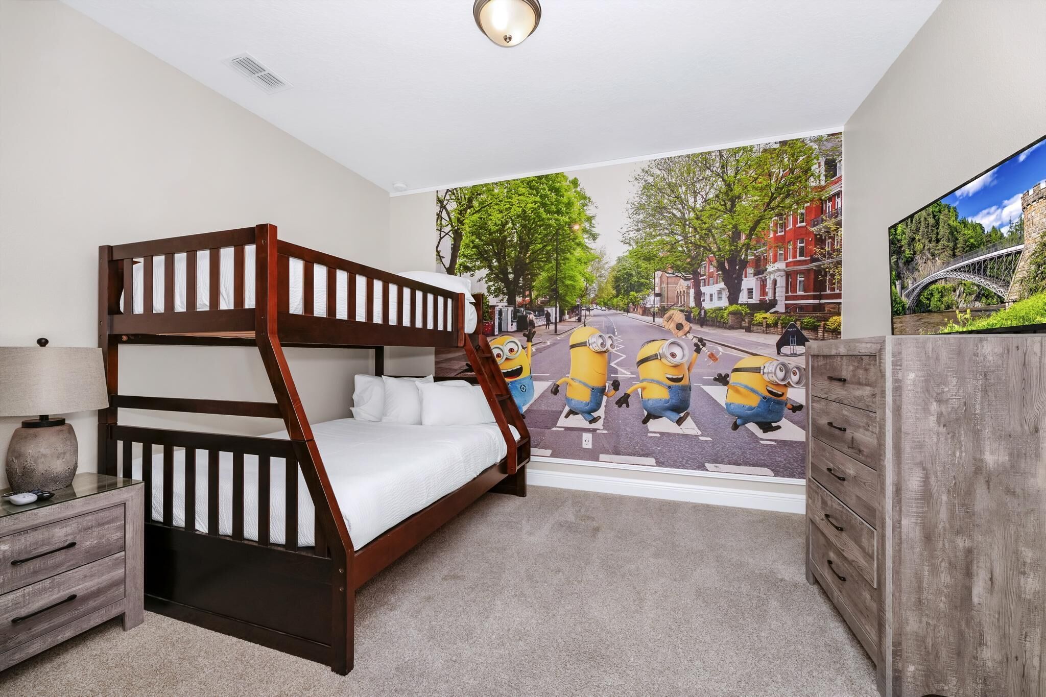 Une chambre avec un lit superposé, une commode, une lampe et une fresque représentant les personnages de « Moi, moche et méchant » sur le mur.