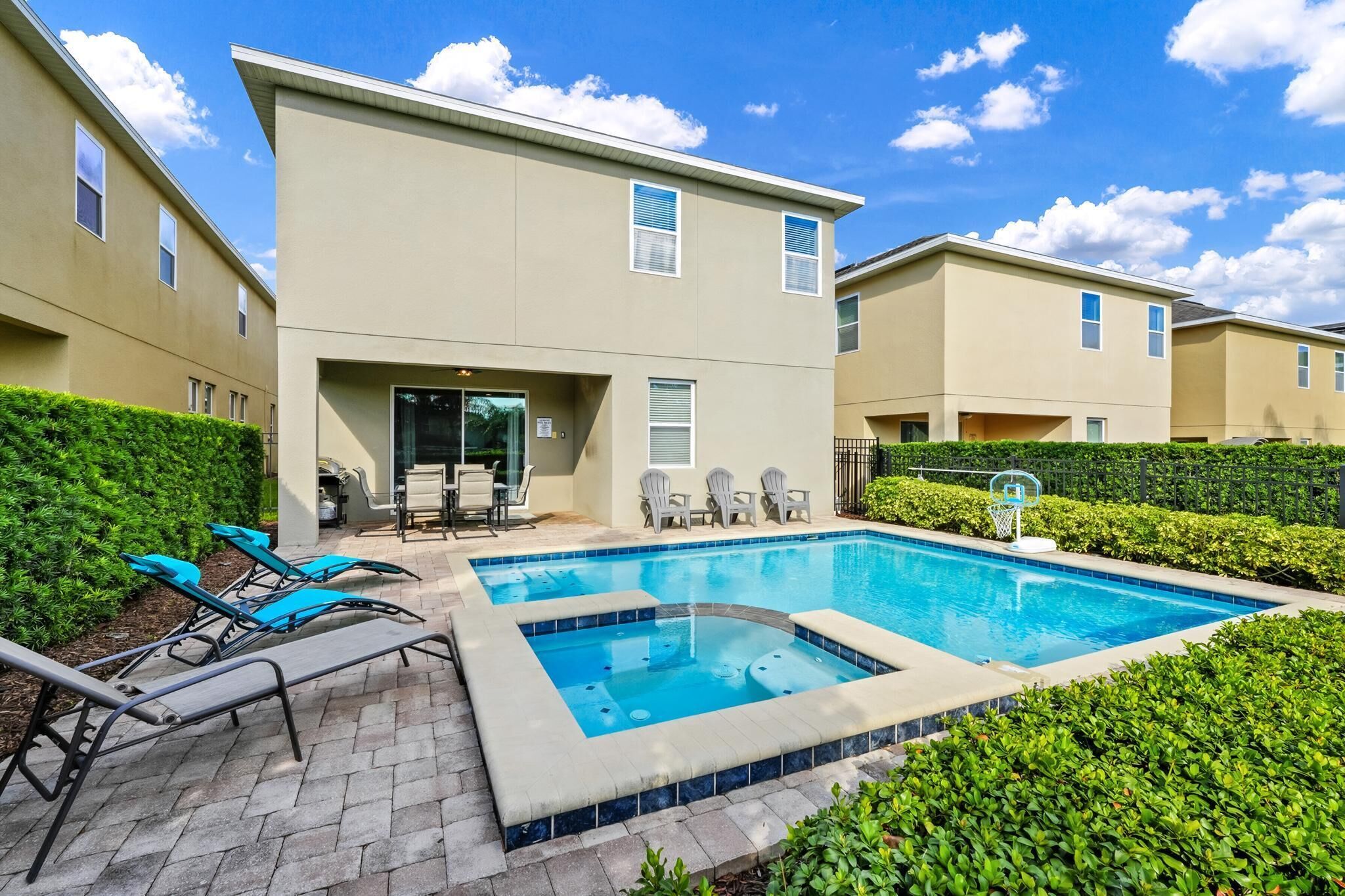 A modern building with a swimming pool, lounge chairs, and a basketball hoop.